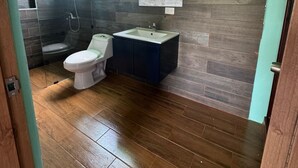 A modern bathroom with a wooden floor, a toilet, a sink, and a shower. - 3-bedroom villa in welcoming Puerto Plata with AC and Fans (puerto plata)