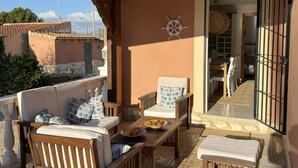 A covered outdoor seating area with wooden furniture, a wall-mounted ship's wheel, and a view of the interior through an open door. - Luxury family villa with private saltwater pool & casita near Alicante (Busot)