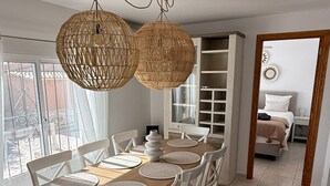 A dining area with a round table, white chairs, woven pendant lights, and a view through a glass door. - Luxury family villa with private saltwater pool & casita near Alicante (Busot)
