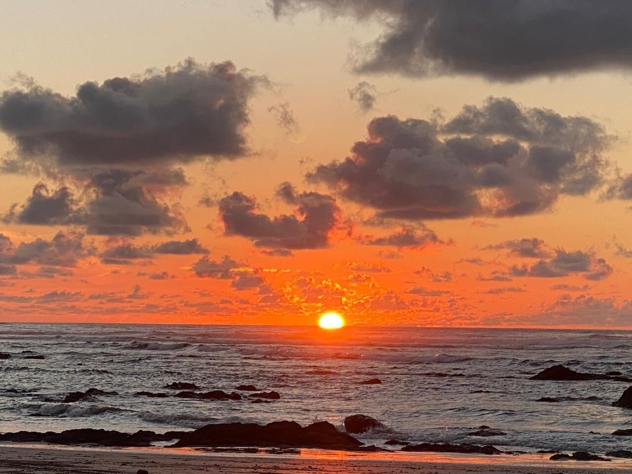 A sunset over the ocean with clouds and rocks in the foreground.