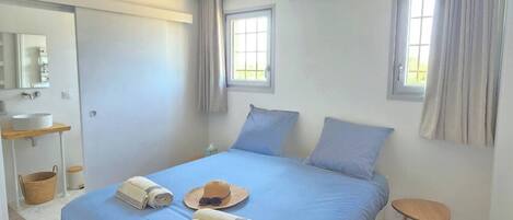 A bedroom with a bed, two windows, a ceiling fan, a bedside table, and a small stool.