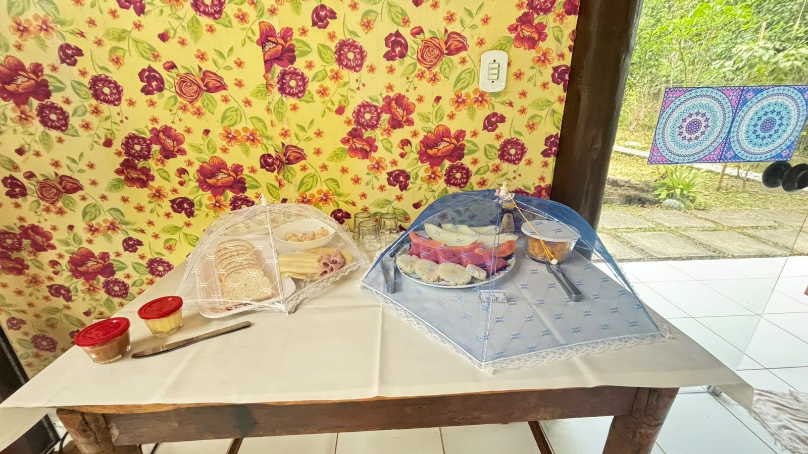 Una mesa con alimentos cubiertos por una red protectora, un cuchillo y dos pequeños recipientes con tapas rojas.
