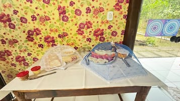 Una mesa con alimentos cubiertos por una red protectora, un cuchillo y dos pequeños recipientes con tapas rojas.