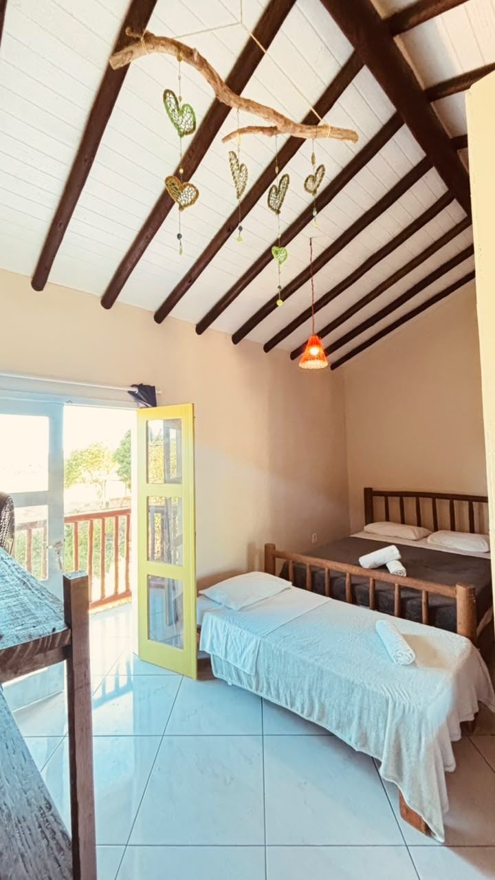 A room with a bed, a table, a hanging heart decoration, and a door leading outside.