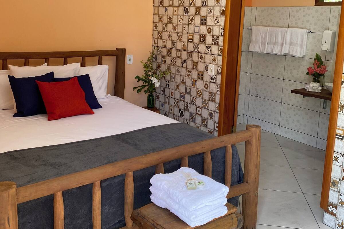 Une chambre d’hôtel comprenant un lit, un banc en bois, une petite table et une salle de bain avec un porte-serviettes.