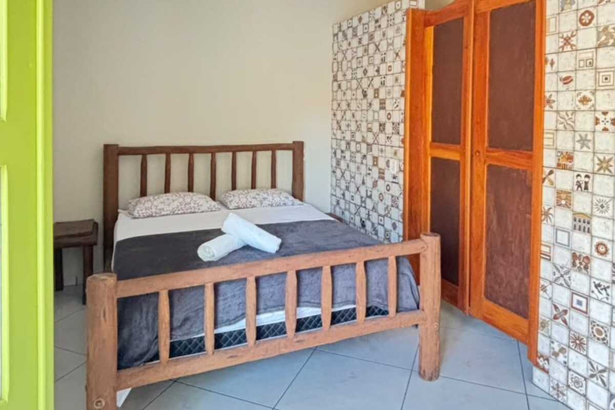 Een slaapkamer met een bed, een houten hoofdbord, een groene deur, een behang met patroon en een betegelde vloer.