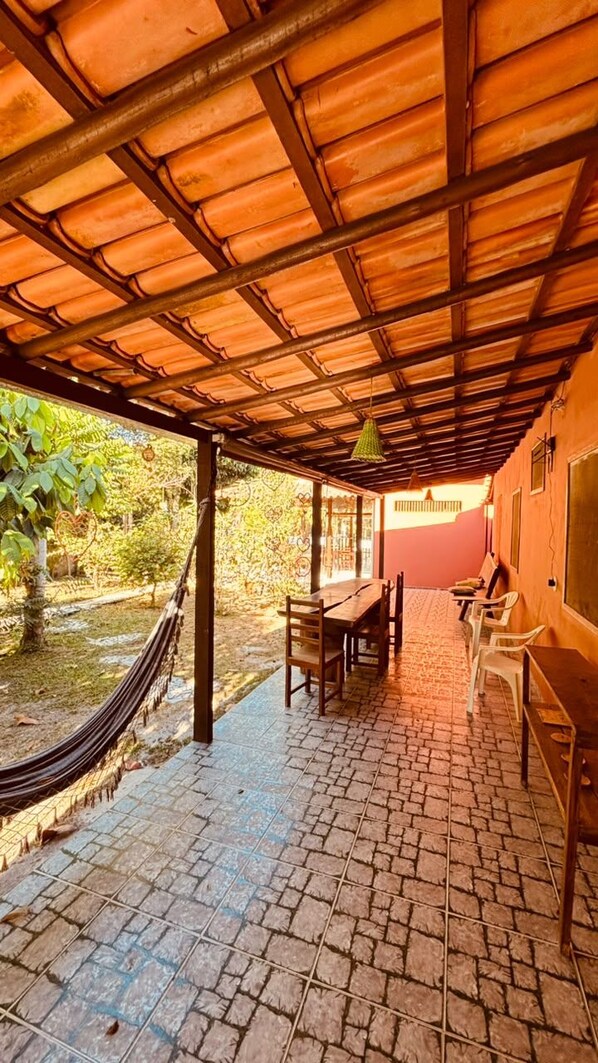 Un patio exterior con suelo de baldosas, una mesa de madera, sillas y una hamaca.