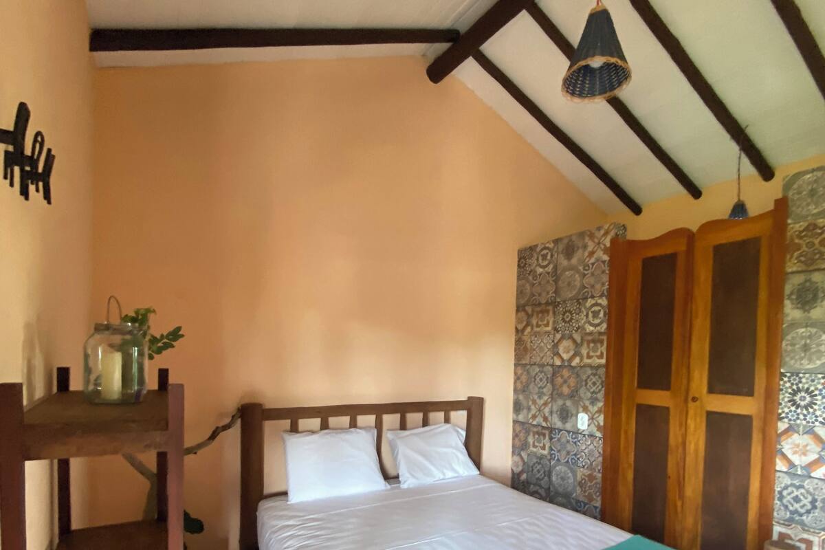 Un lit avec un cadre en bois et une couvre-lit de couleur turquoise, une petite étagère avec une bougie et un luminaire suspendu.