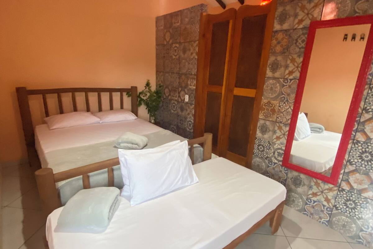 Une chambre avec deux lits en bois, un mur en pierre, un miroir et un luminaire suspendu.