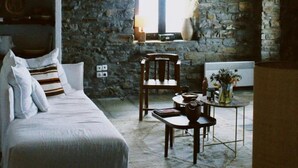 A cozy room with a stone wall, a bed, a table with a vase, and a hanging light fixture. - Kea Infinity View Villa (Kea)