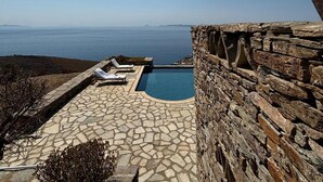 A stone pool with a clear view of the ocean, surrounded by a stone wall and a tiled patio with lounge chairs. - Kea Infinity View Villa (Kea)
