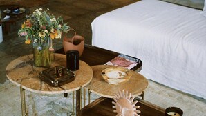 A hotel room with a bed, a round table with a vase of flowers, a tray with a candle, and a small sculpture. - Kea Infinity View Villa (Kea)