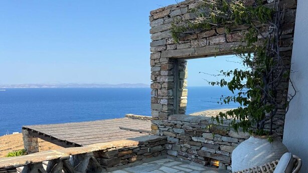 A stone patio with wicker furniture and a view of the sea. - Kea Infinity View Villa (Kea)