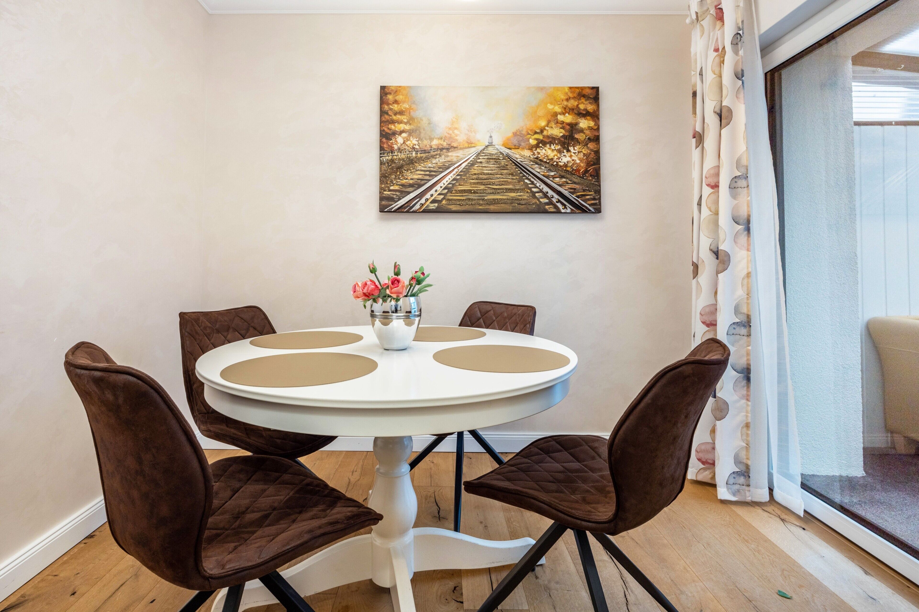 Un coin repas avec une table ronde, quatre chaises, un vase de fleurs et un tableau accroché au mur.