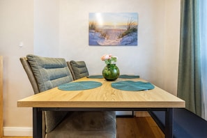 Un'area pranzo con un tavolo in legno, sottopiatti verdi, un vaso con fiori e un quadro raffigurante una spiaggia.