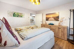 Makuuhuoneessa on sänky, puinen lipasto, auringonlaskua kuvaava taulu ja ovi, joka johtaa toiseen huoneeseen.