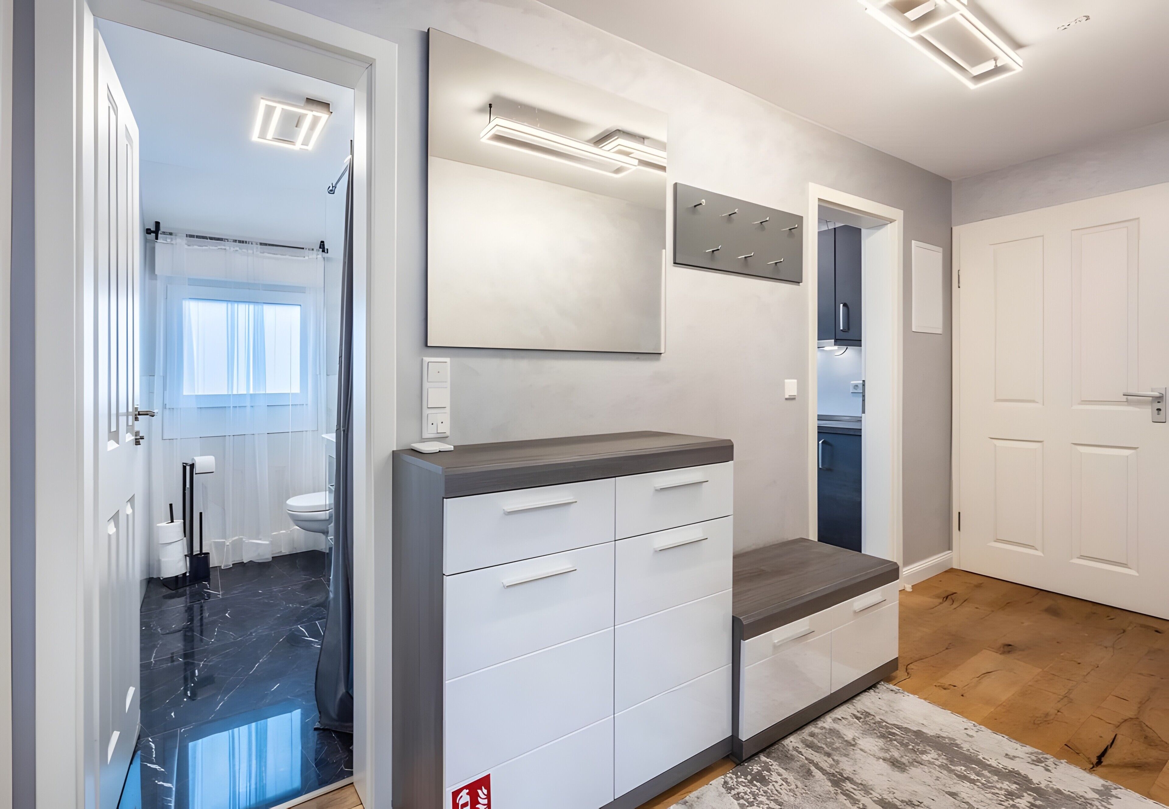 Un baño moderno con un espejo grande, un mueble de tocador con cajones, una zona de ducha y un inodoro.