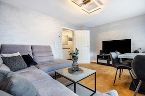 Un salon moderne avec un canapé gris, une table basse, un téléviseur à écran plat et un coin repas avec des chaises.