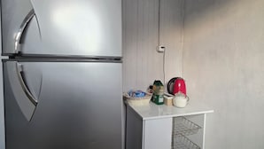 Una cocina con un refrigerador de acero inoxidable, un armario blanco con cestas de alambre y un hervidor rojo sobre la encimera.