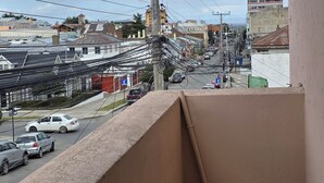 Un balcón con vista a una calle de la ciudad, edificios y coches aparcados.