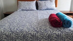 Una cama con colcha estampada de hojas, dos almohadas y dos toallas enrolladas en rojo y azul.