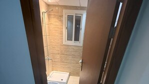 Un couloir étroit mène à une salle de bain équipée d’une douche, de toilettes et d’une fenêtre.