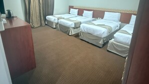 Une chambre d’hôtel avec quatre lits simples, un bureau et une grande fenêtre avec des rideaux.