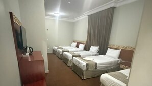 Une chambre d’hôtel avec quatre lits simples, une commode rouge, un téléviseur à écran plat et une grande fenêtre avec des rideaux.