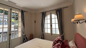 A bedroom with a large bed, two windows with curtains, a wall-mounted lamp, and a view of the outside. - Villa arcachonnaise 8 pers • Beach & center on foot - Quiet garden + parking (Arcachon)