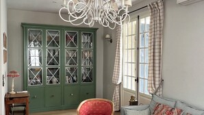 A living room with a wooden coffee table, a red armchair, a grey sofa, a green cabinet, and a white chandelier. - Villa arcachonnaise 8 pers • Beach & center on foot - Quiet garden + parking (Arcachon)