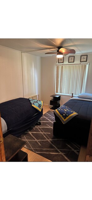 A bedroom with two beds, a ceiling fan, a window with blinds, and a small table with a lamp. - Soothing 3-bedroom farmhouse with AC on 2 acres just outside of Sergeant Bluff (Salix)