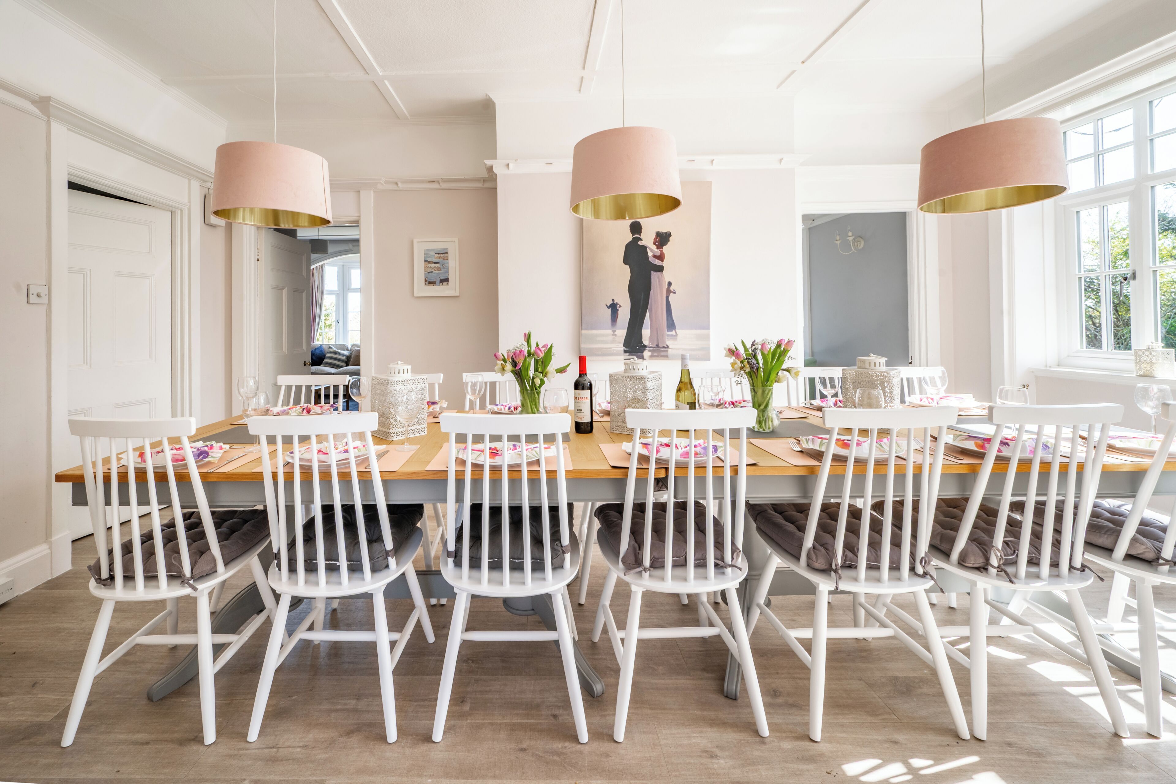 A dining area with a long wooden table, white chairs, and pendant lights.