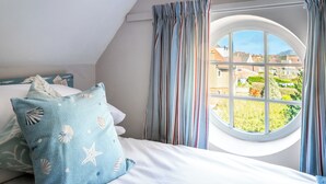 A bedroom with a bed, striped curtains, a round window, and a view of houses.