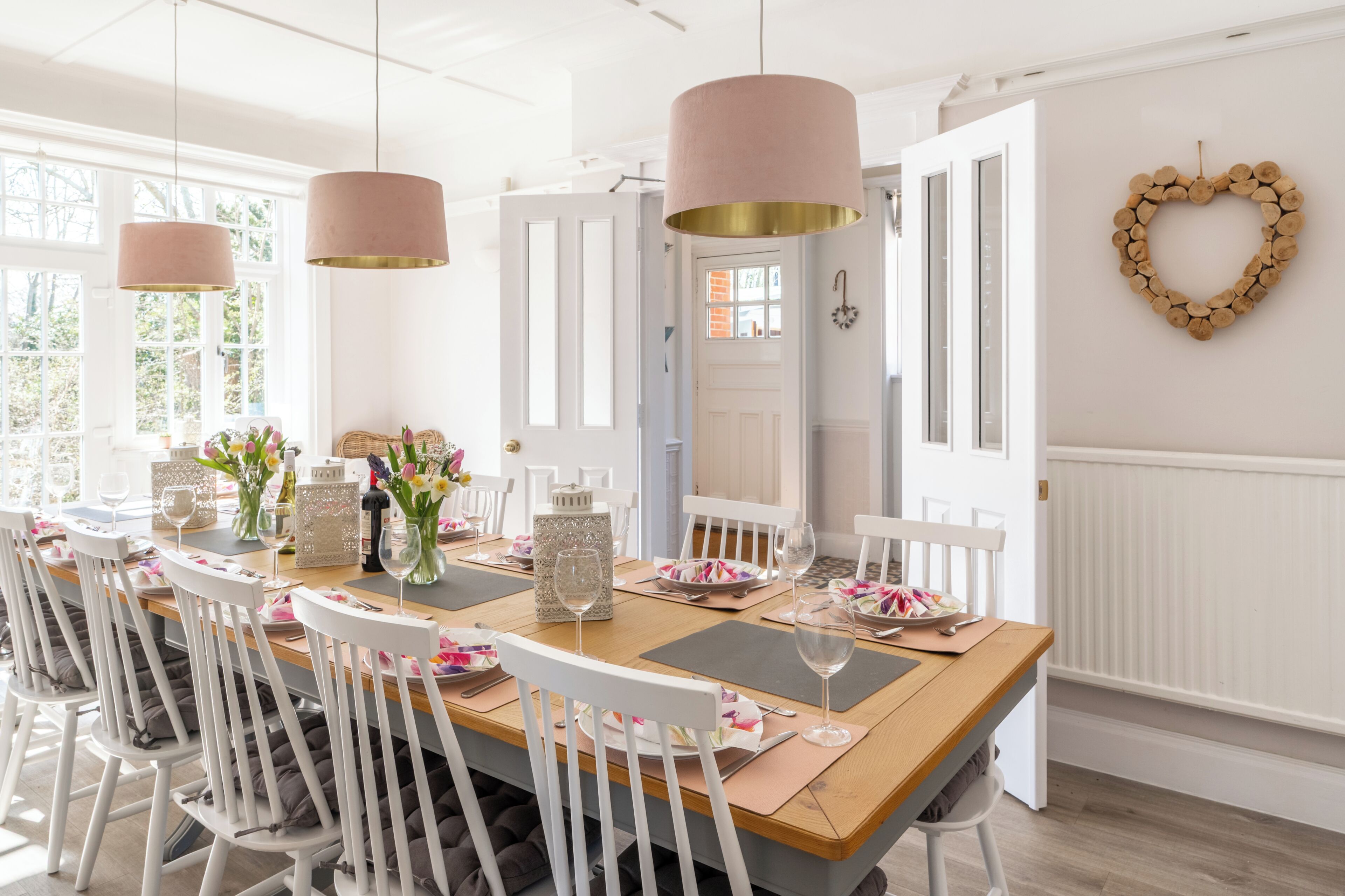 Un espace repas avec une longue table en bois, des chaises blanches et des luminaires suspendus.