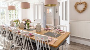 A dining area with a long wooden table, white chairs, and pendant lights.