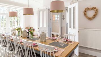 Un espace repas avec une longue table en bois, des chaises blanches et des luminaires suspendus.