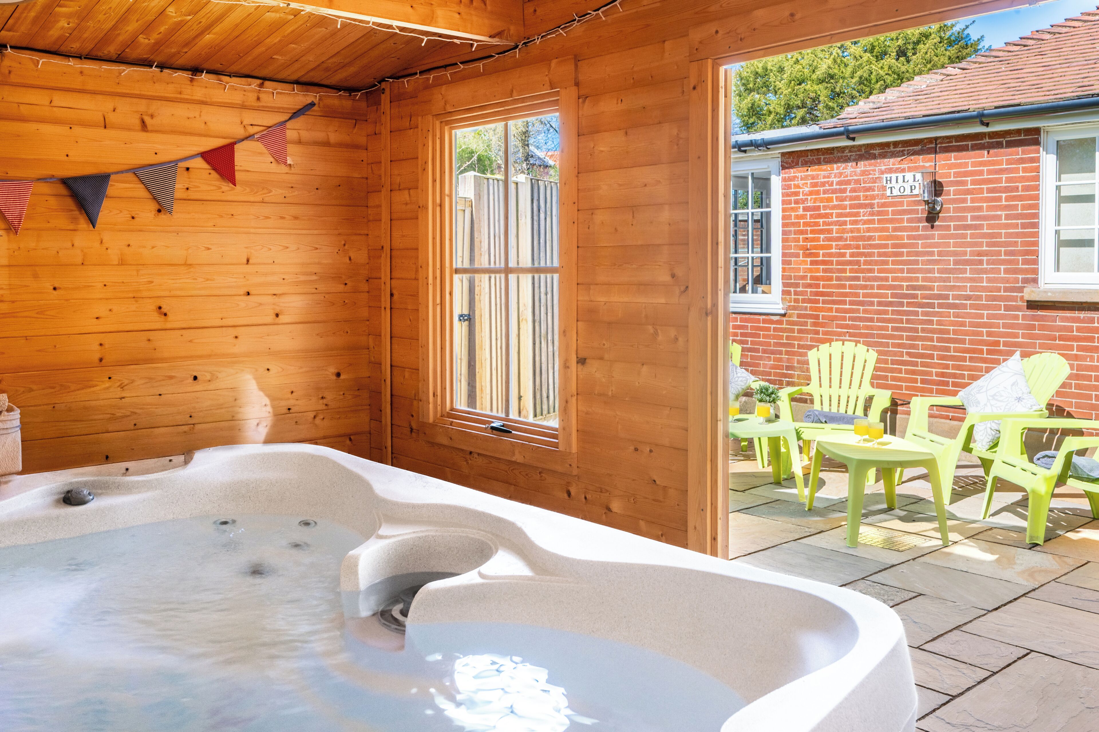 Une cabane en bois dotée d’un bain à remous, de murs en bois, d’une fenêtre et d’une terrasse avec des chaises.