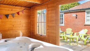A wooden cabin with a hot tub, wooden walls, a window, and a patio with chairs.