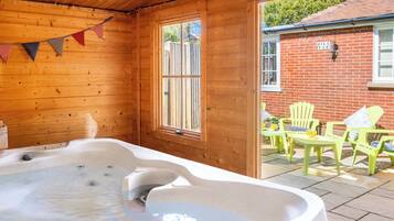 Une cabane en bois dotée d’un bain à remous, de murs en bois, d’une fenêtre et d’une terrasse avec des chaises.