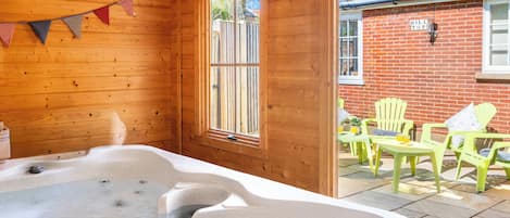 A wooden cabin with a hot tub, wooden walls, a window, and a patio with chairs.