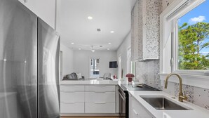 A modern kitchen with a stainless steel refrigerator, white cabinetry, a double sink, and a window with a view of trees. - Kate's House (GuestHouse) (Walton County)
