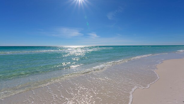 A beach with clear water, a sandy shore, and a bright sun in the sky. - Kate's House (GuestHouse) (Walton County)