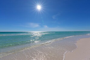 A beach with clear water, a sandy shore, and a bright sun in the sky. - Kate's House (GuestHouse) (Walton County)