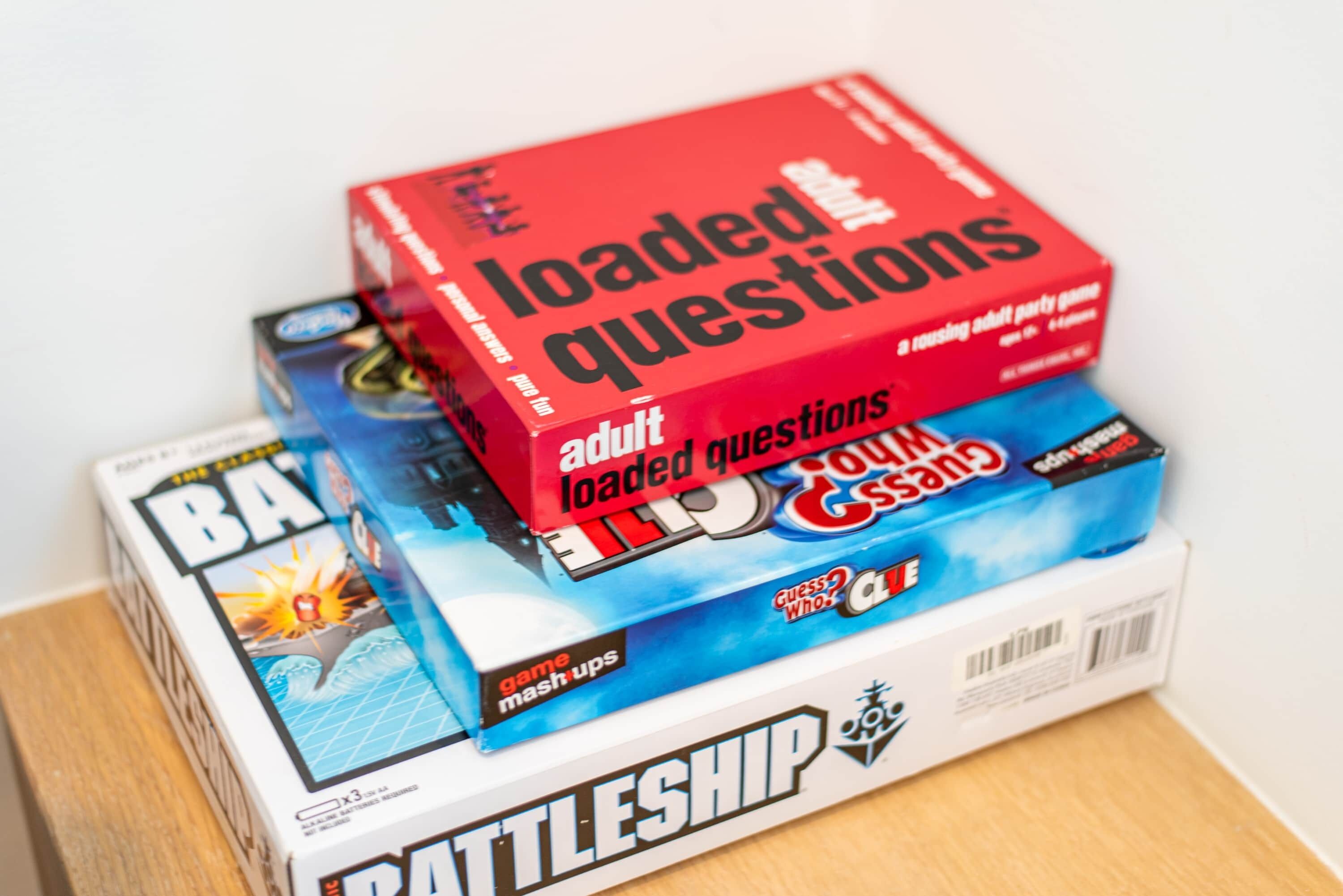 A stack of board games including 'Loaded Questions' and 'Battleship' on a table.