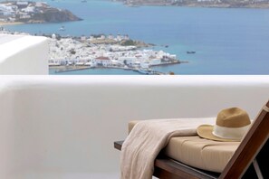 A balcony with a view of a coastal town, a hat, and a blanket on a chair. - Mykonos Seaview Villa Alea (Mykonos)