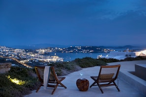 Two wicker chairs with cushions on a rooftop terrace overlooking a cityscape at dusk. - Mykonos Seaview Villa Alea (Mykonos)