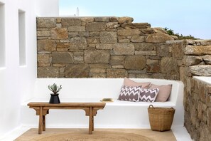 A white bathtub with a stone wall backdrop, a wooden bench, a potted plant, and a wicker basket. - Mykonos Seaview Villa Alea (Mykonos)