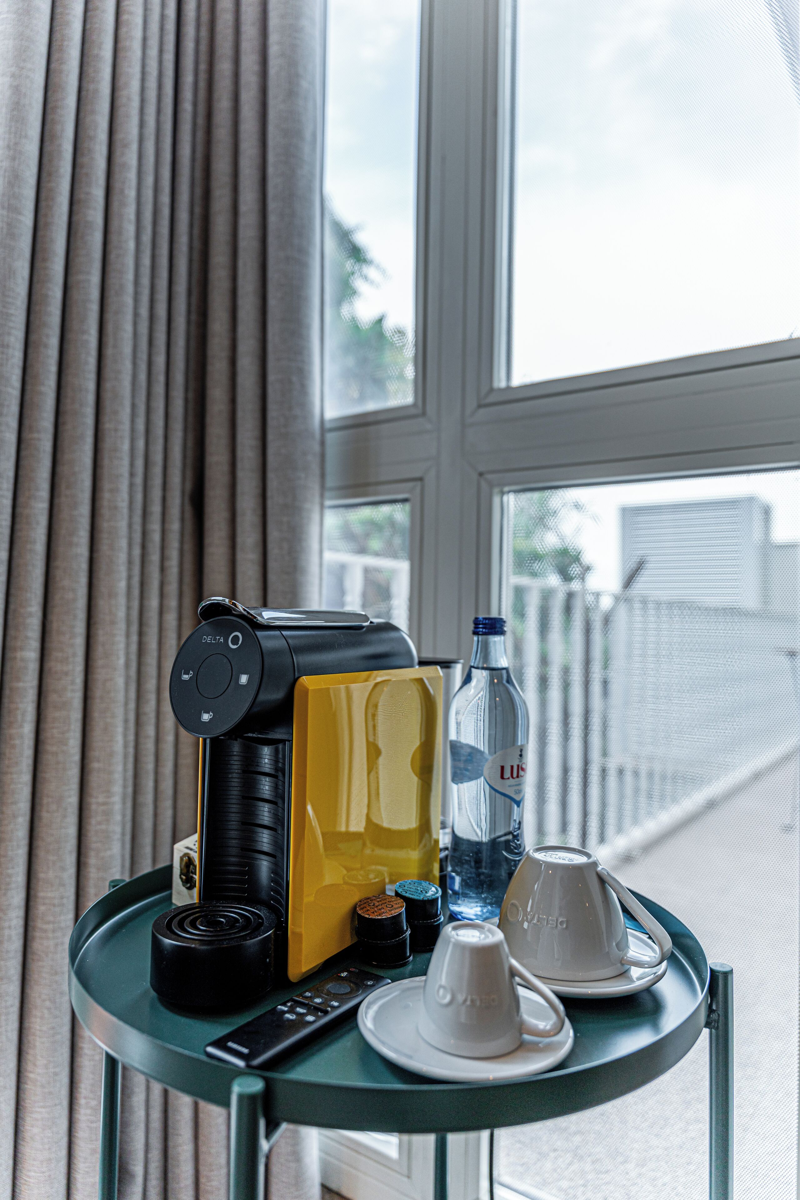 Une table avec une machine à café, une boîte jaune, une bouteille d’eau et deux tasses.