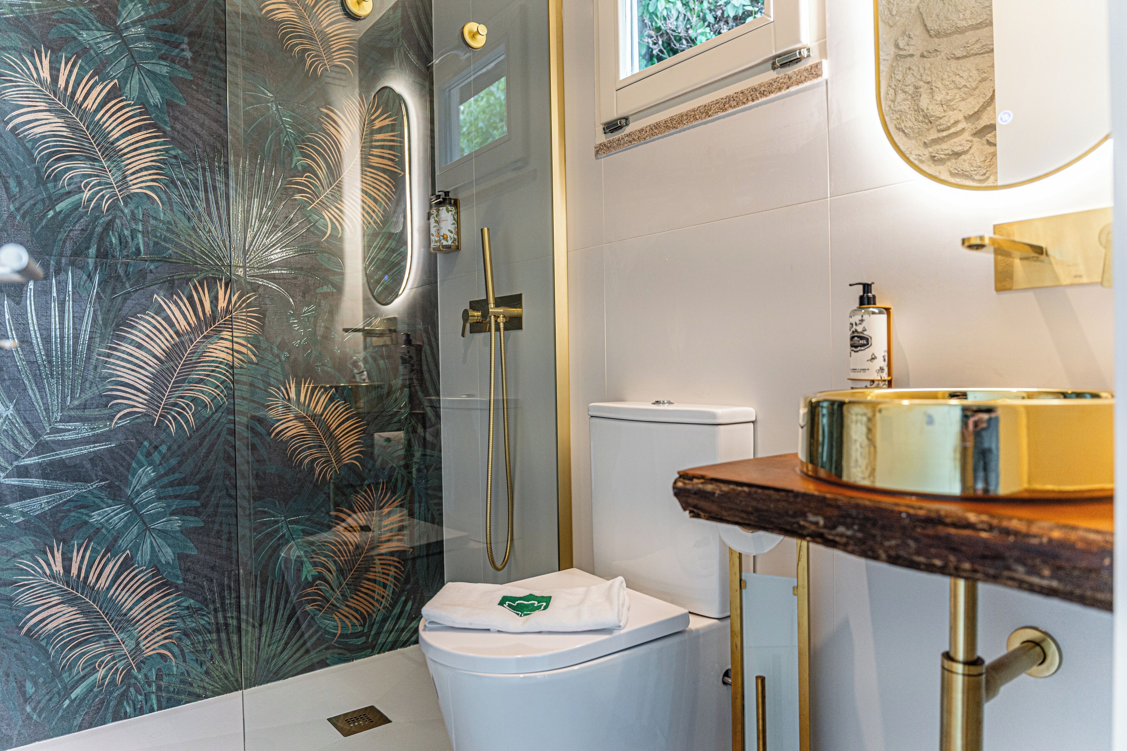 Un baño moderno con cabina de ducha de vidrio, inodoro blanco y tocador de madera con lavamanos dorado.
