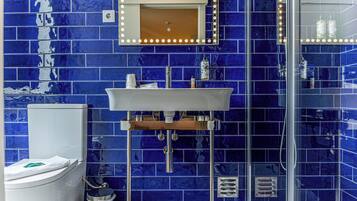 A bathroom with a blue-tiled wall, a white sink, a mirror with lights, and a glass shower enclosure.